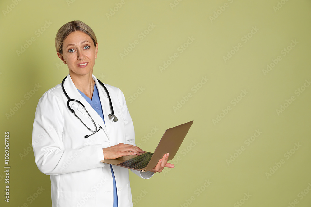 Doctor in medical uniform with stethoscope and laptop on light green background, space for text Doctor in medical uniform with stethoscope and laptop on light green background, space for text