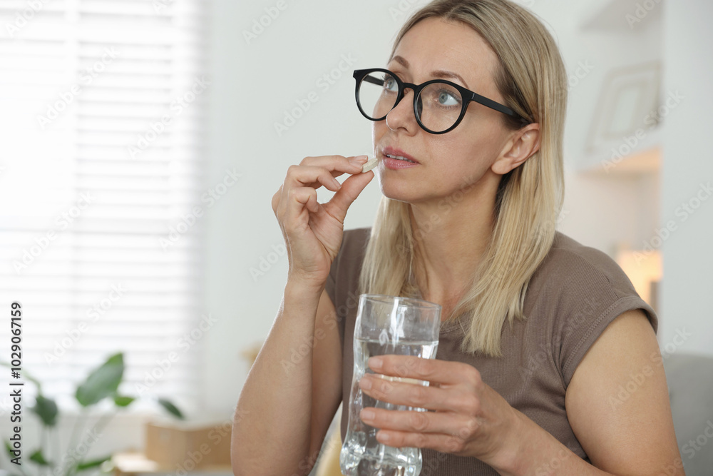 Menopause, hormone replacement therapy. Woman with glass of water taking pill at home, space for text Menopause, hormone replacement therapy. Woman with glass of water taking pill at home, space for text