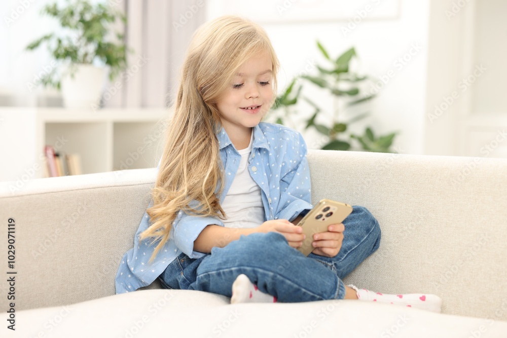 Cute little girl using smartphone on sofa at home Cute little girl using smartphone on sofa at home