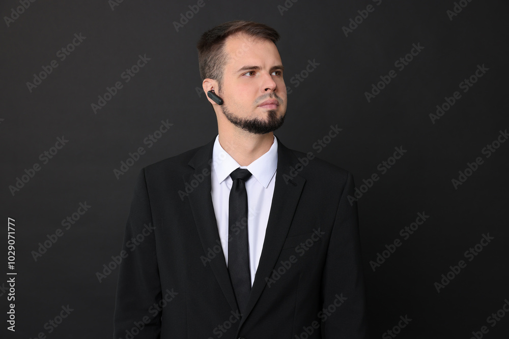 Young bodyguard in suit with earpiece on black background Young bodyguard in suit with earpiece on black background