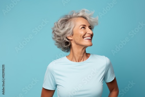 Portrait of a happy woman in her 50s wearing a moisture-wicking running shirt while standing against pastel blue background