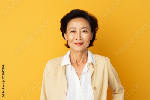 Portrait of a glad asian woman in her 60s wearing a classic white shirt in pastel yellow background photo