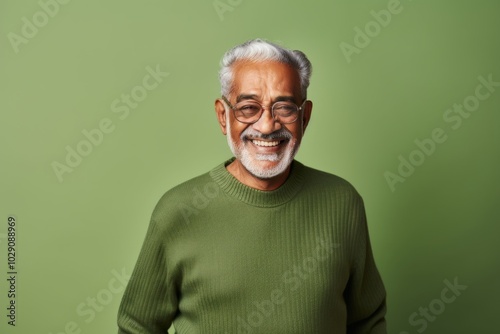 Portrait of a content indian elderly man in his 90s wearing a cozy sweater while standing against pastel green background