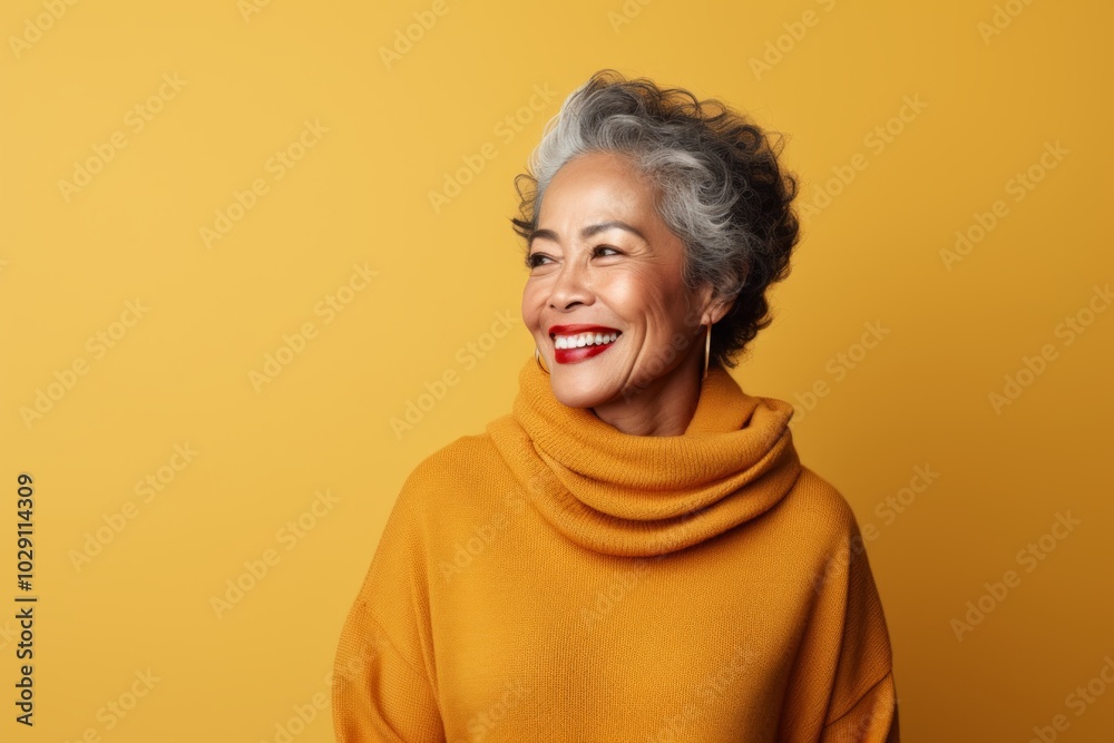 Fototapeta premium Portrait of a joyful woman in her 70s dressed in a comfy fleece pullover over soft yellow background