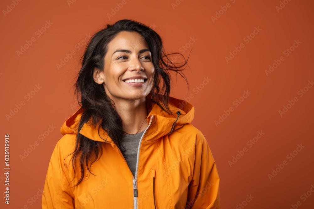 Portrait of a blissful indian woman in her 40s wearing a functional windbreaker isolated on soft orange background Portrait of a blissful indian woman in her 40s wearing a functional windbreaker isolated on soft orange background