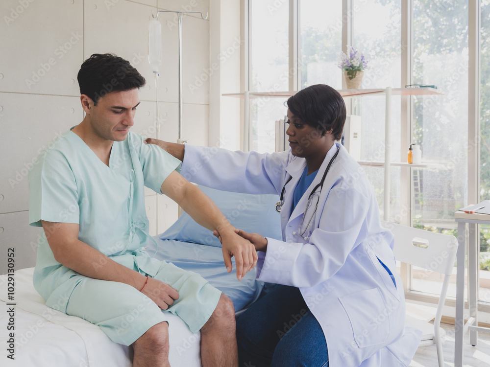 Patient caucasian man with woman nurse carer physical therapist black people two person sitting talk helping support give advice and holding hand arm inside clinic hospital indoor room service. Patient caucasian man with woman nurse carer physical therapist black people two person sitting talk helping support give advice and holding hand arm inside clinic hospital indoor room service.