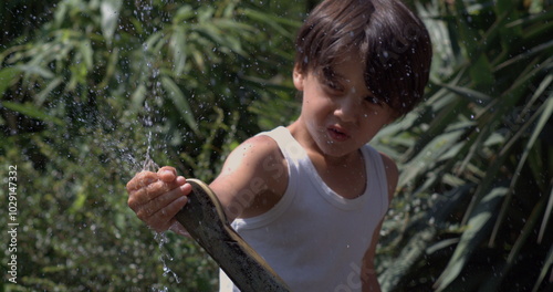 Child smiling and playing with water splashes in slow motion at 800 fps, enjoying the outdoor fun on a sunny day photo