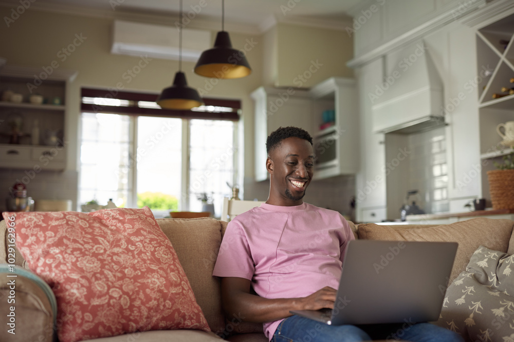 Smiling young African man using a laptop on his living room sofa Smiling young African man using a laptop on his living room sofa