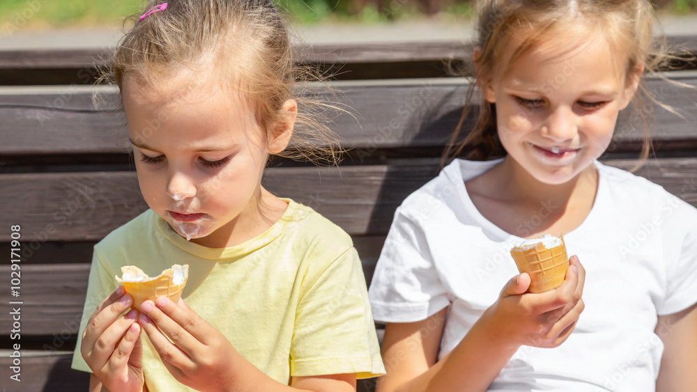 Happy children eating ice cream together outdoor. Photo of happy girls sitting on the bench and smiling at camera. Happy children eating ice cream together outdoor. Photo of happy girls sitting on the bench and smiling at camera.