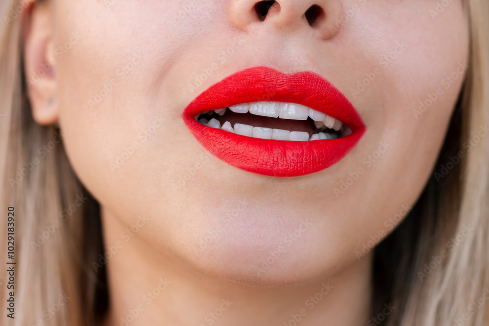 Fototapeta premium Close up of a young attractive caucasian blonde woman with her mouth slightly open with matte red color lipstick. Beauty and fashion concept