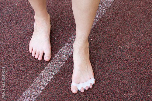 Close-up of female bare feet standing on a textured surface. The feet are wearing in silicone toe separators, promoting toe alignment and foot health. Self-care procedures for healthy feet.