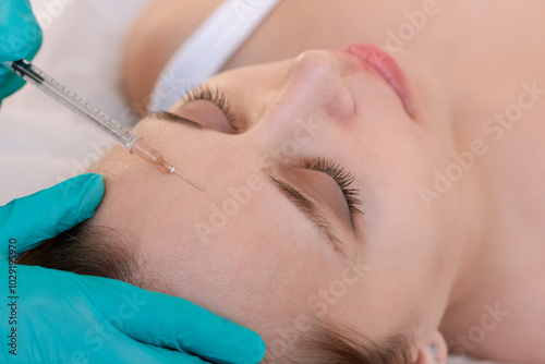 Close up of young woman and doctor's hands in gloves holding syringe for injection the botulinum toxin into the forehead. Face lift. Anti-aging treatment. Skin care. Getting rid of facial wrinkles 