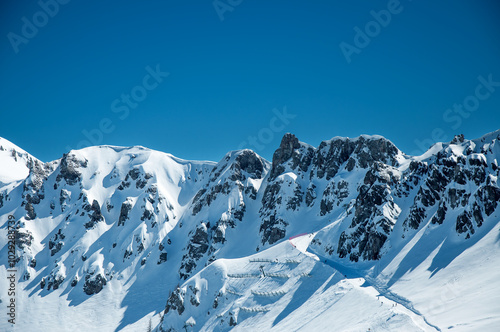 Dolomites, Italy. Arabba ski resort. Mountain range with ski piste, run and slope with unrecognizable skiers. Very steep ski lift and avalanche fences. Blue sky with big copy space. Winter landscape