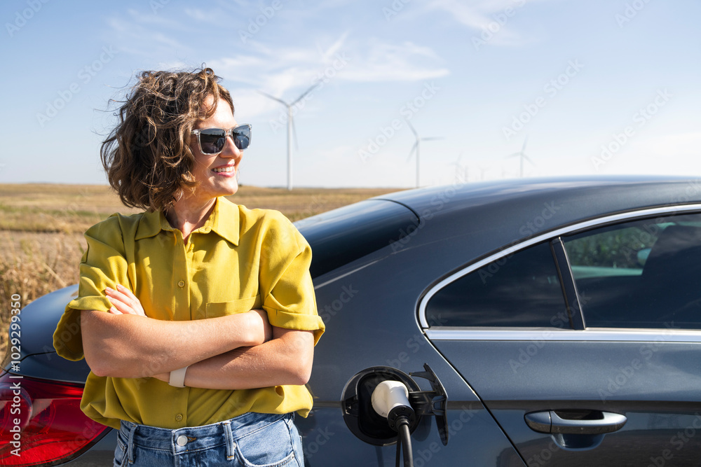 Φωτογραφία Woman with curve hairs wearing yellow shirt and sunglasses stands next to charging electric car