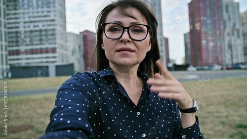 Selfie view middle aged woman, talking on webcam, urban style