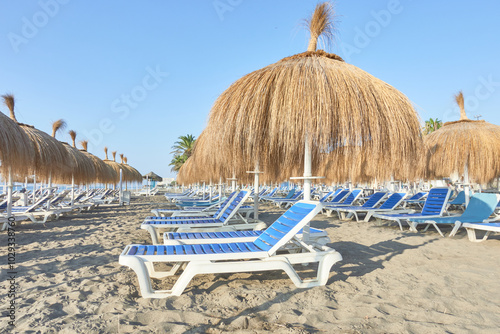 Row of blue and white sun loungers with straw parasols on the sand of a beach in Torremolinos, Malaga, Andalusia, Spain