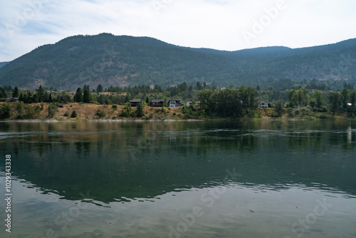 Serene river landscape with reflections of mountains and trees in the soft light of a summer afternoon near a quiet residential area