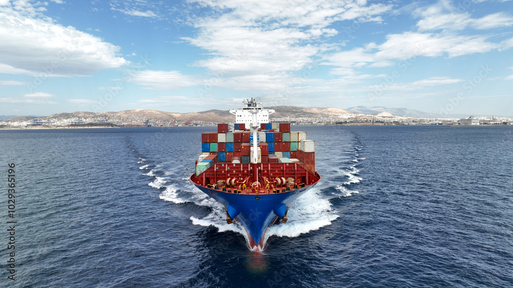 Aerial drone photo of colourful truck size container tanker ship cruising deep blue sea near commercial port of Piraeus, Attica, Greece