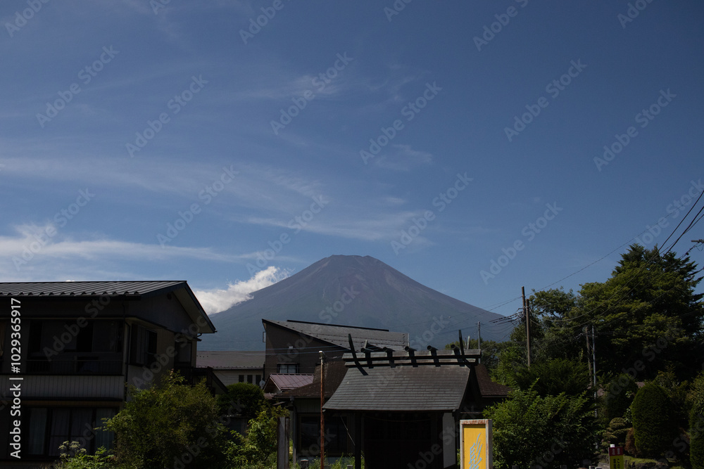 This is a beautiful image of Mount Fuji stretching up into the clear blue sky. White clouds can be seen around the base being blocked. This was shot in Fujiyoshida Japan among the town. This is a beautiful image of Mount Fuji stretching up into the clear blue sky. White clouds can be seen around the base being blocked. This was shot in Fujiyoshida Japan among the town.