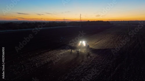 Agriculture and agribusiness. Aerial Tractor with lights on sowing seeds late into the night. Night shift for tractor drivers