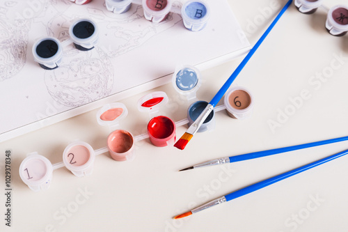 Fototapeta Naklejka Na Ścianę i Meble -  Brush dipped in red acrylic paint and containers with paints for painting a picture