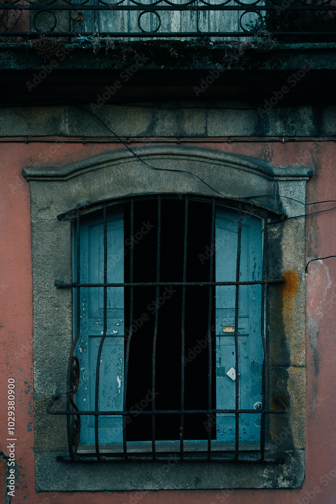 Obraz premium An old window with bars on the facade of a worn building.