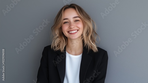 Young woman with wavy hair smiling in casual attire against a gray background during daylight