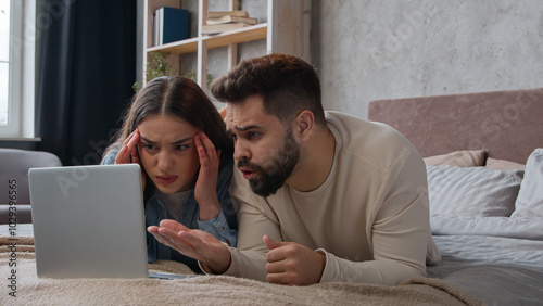 Desperate stressful Caucasian sad couple homeowners confused family wife husband read bad email trouble lost bank mortgage negative result computer failure anxious man and woman lying on bed at home