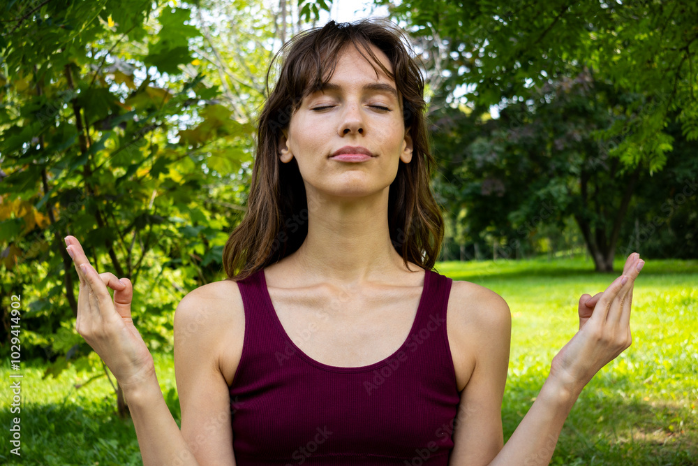 Portrait of the beautiful brunette doing yoga and showing mudras in the green park in summer Portrait of the beautiful brunette doing yoga and showing mudras in the green park in summer