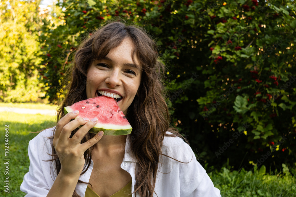 Happy curly brunette laughing and eating watermelon in the park in summer Happy curly brunette laughing and eating watermelon in the park in summer