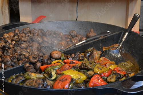 Grande casserole dans laquelle est cuisinée des légumes, poivrons rouges et verts et des champignons