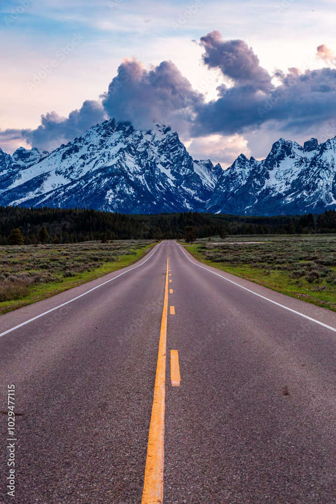 Fototapeta premium Lonely Road Leading to Majestic Grand Teton Mountains at Sunset