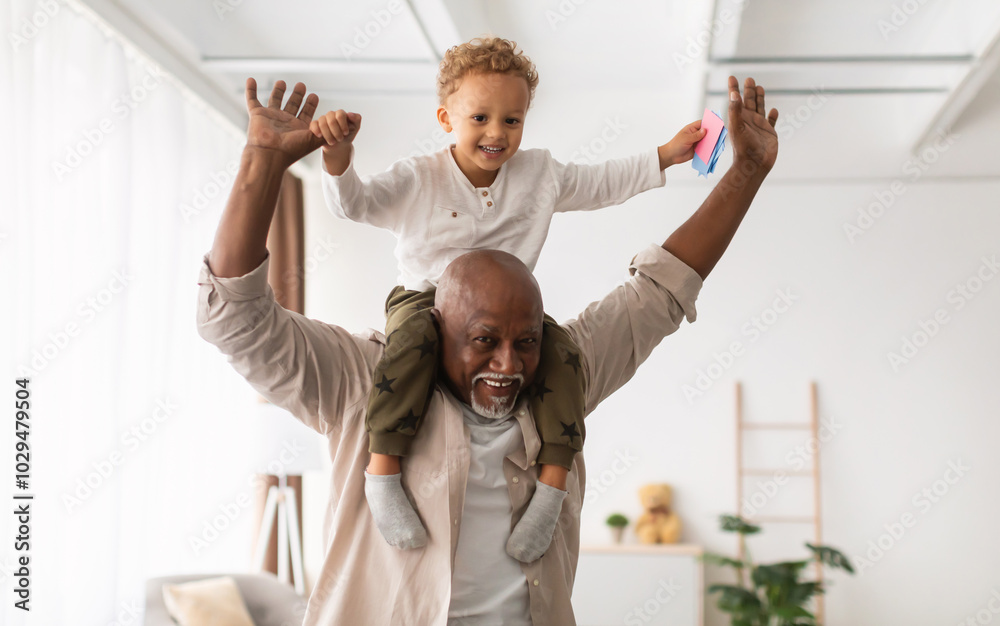 Obraz premium Best Grandfather. Cheerful Black Grandpa Carrying Little Grandson On Shoulders Playing And Having Fun Together At Home. Grandparent Spending Time With Happy Grandchild On Weekend