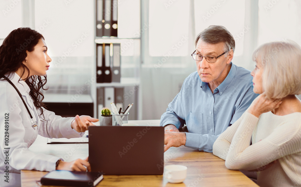Medical Test Results. Brazilian doctor pointing at digital tablet, explaining diagnosis to senior couple, copyspace Medical Test Results. Brazilian doctor pointing at digital tablet, explaining diagnosis to senior couple, copyspace