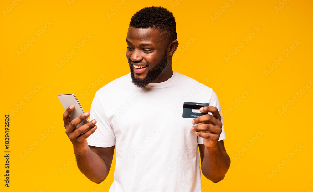 Online payment. Cheerful black man using credit card and smartphone for purchasing goods Online payment. Cheerful black man using credit card and smartphone for purchasing goods