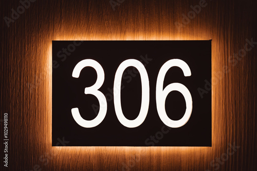 Close-up of a room number 306 on wooden background in hotel. Illuminated and casting a soft glow sign. Arabic numerals three zero six.