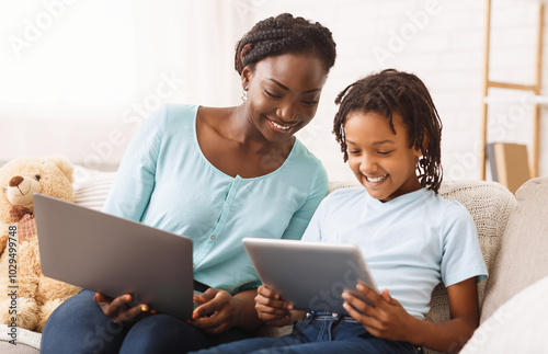 Black Mother Helping Daughter With Homework, Studying Together Using Digital Tablet And Laptop photo