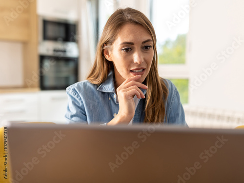 Young woman working on laptop at home in front of kitchen