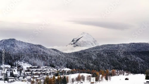 Big white mountain peak covered in fresh white snow above vibrant clouds settling below with an alpine Austrian village below in the Alps