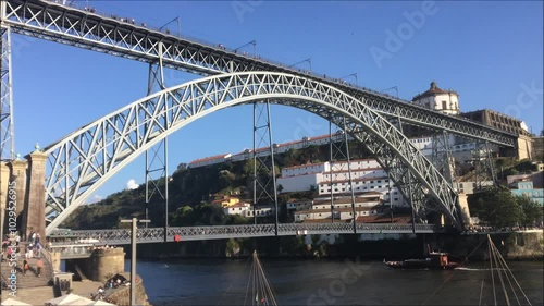 Downtown Porto city with Dom Luís bridge, people in motion, tourist boats passing in Rio Douro and metro at the top of the bridge