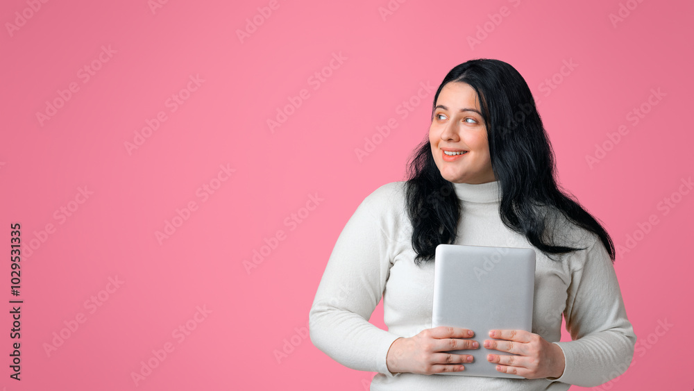 Online education concept. Smiling plus sized girl holding digital tablet and looking aside at free space on pink background, panorama Online education concept. Smiling plus sized girl holding digital tablet and looking aside at free space on pink background, panorama