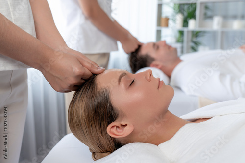 Caucasian couple enjoying relaxing anti-stress head massage and pampering facial beauty skin recreation leisure in dayspa modern light ambient at luxury resort or hotel spa salon. Quiescent