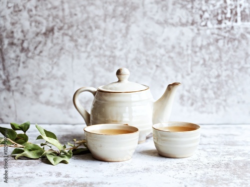 Wallpaper Mural A traditional ceramic teapot with two cups and greenery on a rustic textured surface in a cozy setting Torontodigital.ca
