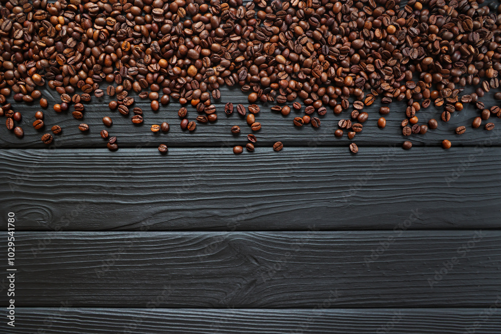 Fototapeta premium Coffee beans scattered on dark wooden surface. A top-down view of roasted coffee beans spread across a dark textured wooden surface.