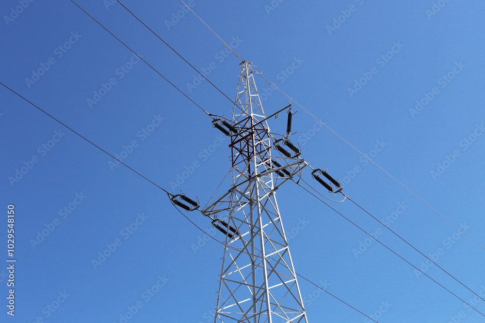 Transmission tower against a clear blue sky. High voltage electricity pylon standing tall. Metal construction with power lines extending into the distance. Energy distribution infrastructure and steel Transmission tower against a clear blue sky. High voltage electricity pylon standing tall. Metal construction with power lines extending into the distance. Energy distribution infrastructure and steel