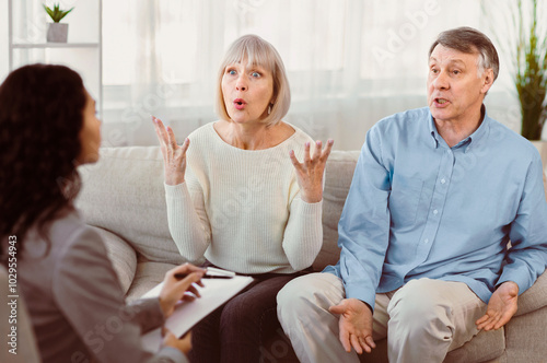 Marriage Therapist. Angry mature wife talking to psychologist sitting on couch with husband, sharing marital problems