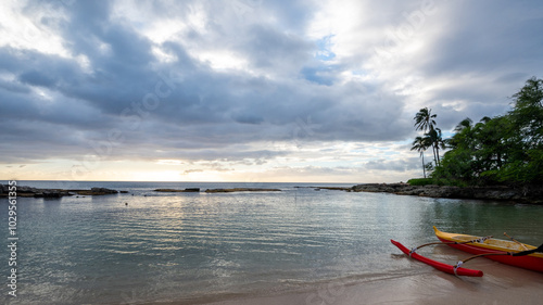 As the sun sets, two individuals paddle in a kayak on a peaceful beach while dark clouds loom overhead, reflecting the day's last light on the water's surface.