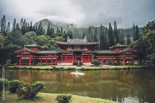A traditional Japanese temple nestled in lush greenery next to a serene pond under cloudy skies in a tranquil landscape