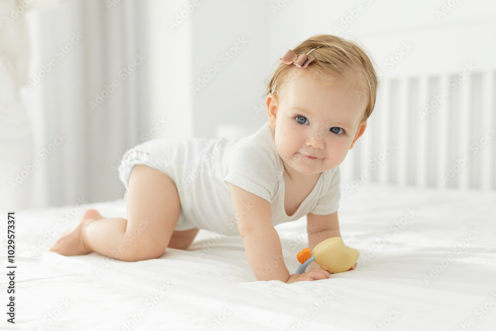 Cute little baby girl learning to crawl and playing with toy on white bed at home, kid woke up in the morning. Happy childhood concept Cute little baby girl learning to crawl and playing with toy on white bed at home, kid woke up in the morning. Happy childhood concept