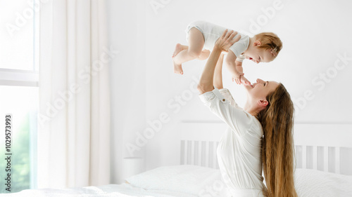 Happy young mother raising her adorable baby girl in air, playing with kid, enjoying motherhood, maternity leave, panorama with free space